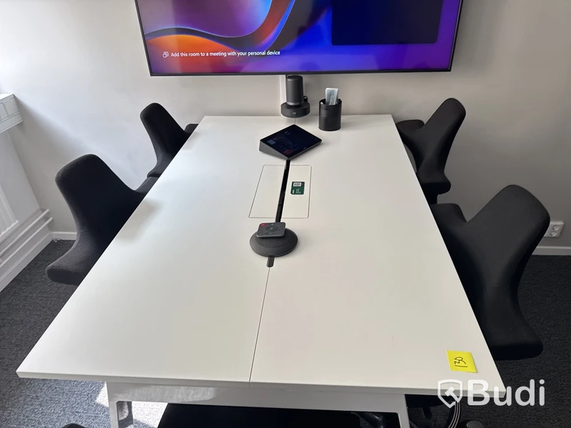 Konferensrum med bord, stolar, skärm och konferensutrustning