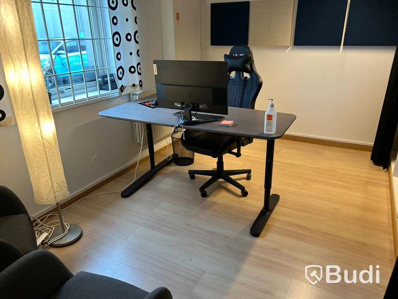 Kontorsrum med skrivbord, stol, datorskärm, besöksstolar med litet bord, ljudabsorbenter