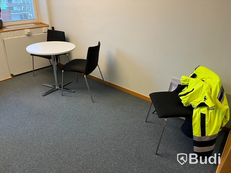 Kontorsrum, vitt skrivbord, stol, vitt skåp, besöksstolar med bord, dragskjutskåp