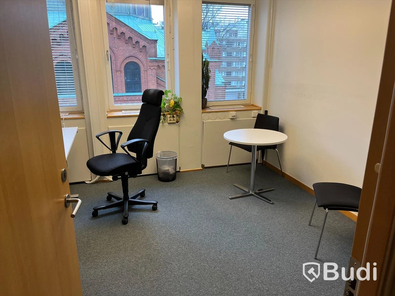 Kontorsrum, vitt skrivbord, stol, vitt skåp, besöksstolar med bord, dragskjutskåp