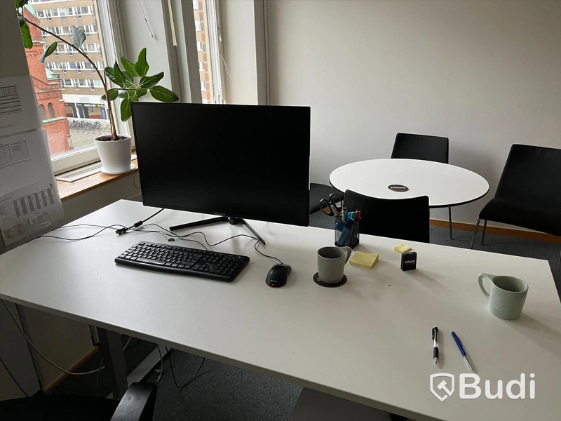 Kontorsplats, höj- & sänkbart skrivbord, stol, datorskärm, bokhylla, besöksbord med stolar