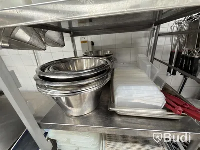 Two stainless steel shelves with assorted stainless steel kitchen accessories and oven drawers