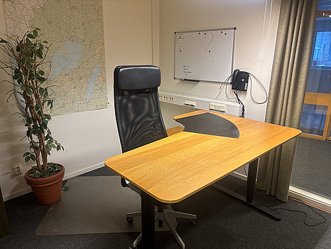 Kontorsplats med skrivbord, stol och hylla.